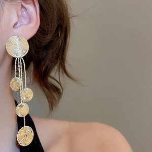 Close-up of golden tassel earrings with five tiered discs and radial texture on a model