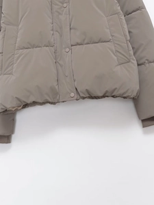 Detail of taupe quilted puffer jacket hem featuring snap buttons and ribbed cuffs
