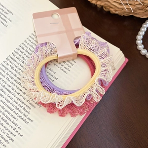Détail de trois chouchous avec bordure en dentelle en violet, beige et rose sur carte
