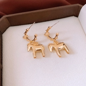 Detailed close-up of golden horse pendant earrings in a white jewelry display box
