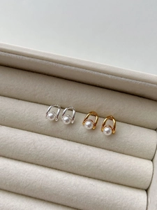 Detailed view of gold and silver minimalist U-shaped pearl stud earrings on velvet