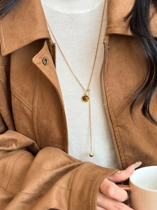 Close-up of golden Y-shaped tiger eye pendant necklace on a brown suede jacket