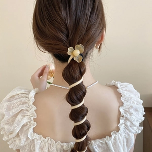 Détail d'élastique fleur jaune et d'un bandeau spirale crème sur une tresse en queue de cheval