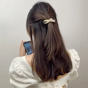 Detail of a gold-tone bow hair clip with white pearls on a model with long brown hair