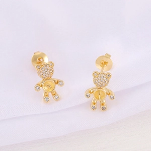 Macro detail of gold-plated bear stud earrings with zircon stones on white fabric