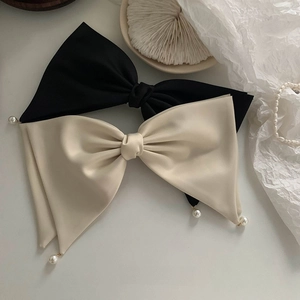 Detailed view of satin bow hair clips with pearl accents in black and off-white colors