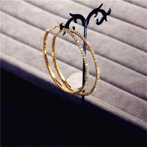 Detailed close-up of oversized gold crystal hoop earrings on a black display stand