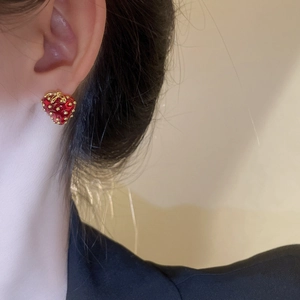 Close-up of a red strawberry stud earring with gold leaf details on a model's ear