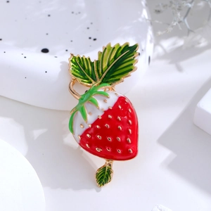 Cute strawberry enamel brooch with vibrant red and green colors on a ceramic tray