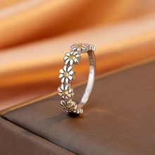 Macro shot of silver daisy chain ring with yellow centers on golden silk background