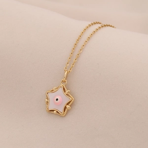 Dettaglio del ciondolo a stella rosa con occhio e catena d'oro su tessuto beige