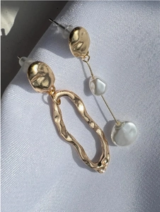 Detailed view of asymmetric gold earrings with baroque pearls on white silk fabric