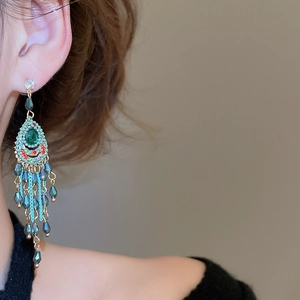 Detail of bohemian drop earrings with emerald crystal and light blue beaded tassels
