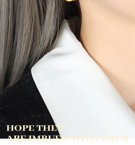 Detail of trendy gold oval earring paired with chic black tweed and white satin fabric