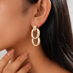 Macro detail of gold interlocking oval earrings with zircons on model's ear