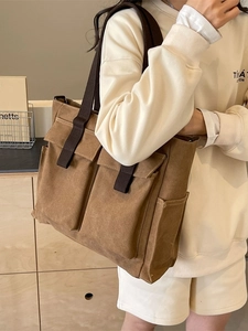 Borsa tote in tela marrone con tasche frontali indossata da una modella in abbigliamento casual