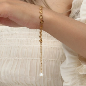Close-up of golden heart-shaped bracelet with pearl pendant on a woman's wrist