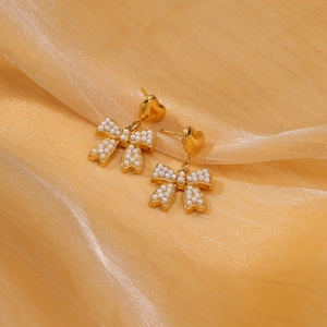 Close-up of golden heart-shaped hook earrings with pearl bow charms on silk background