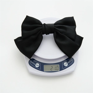 Weight measurement of a black satin bow hair clip on a digital scale showing 21.0g