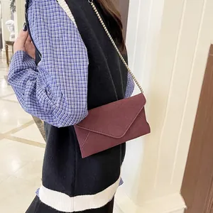 Elegant wine red suede crossbody bag with gold chain strap shown on a model