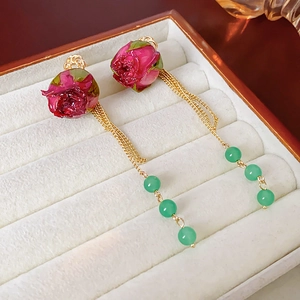 Detailansicht langer Ohrringe mit roten Rosen, Goldketten und grünen Perlen auf Samt