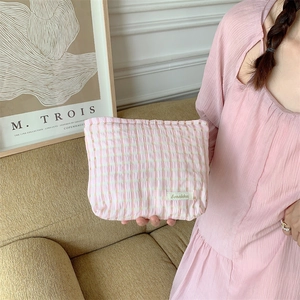 Detailed view of pink plaid fabric cosmetic bag with Sorakka label held by a person