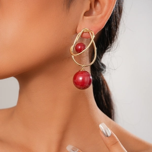Macro shot of gold geometric earrings featuring asymmetric lines and red resin beads
