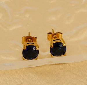 Macro shot of 18k gold plated round earrings with blue zircon on silk texture