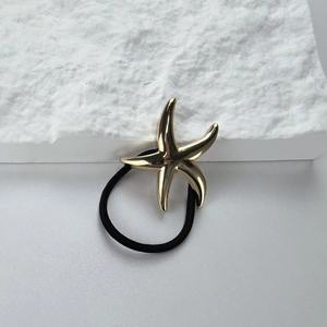 Detail of golden metal starfish charm on a high-elastic black hair tie for ponytail styling