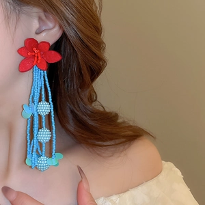 Detail of long red floral earrings with light blue seed bead tassels on a female model