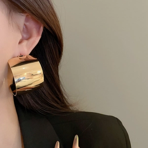 Close-up of chunky gold-plated wide hoop earrings on model with high-polish finish