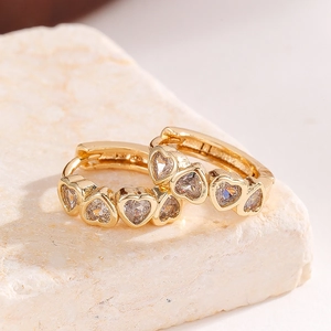Macro detail of gold-plated heart hoop earrings with cubic zirconia on a stone base