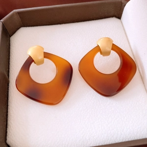 Vue macro de boucles d'oreilles carrées en acétate d'ambre dans un écrin à bijoux