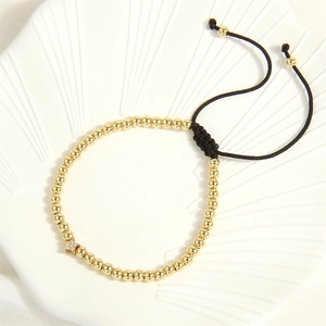 Detail of gold beaded bracelet with star charm and black braided adjustable cord