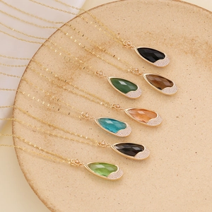 Golden teardrop necklaces with colorful crystal stones arranged on a ceramic tray