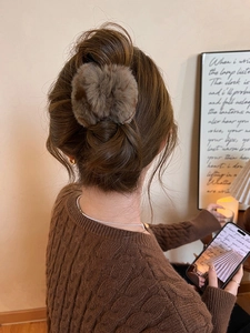 Gros plan sur la pince à cheveux en peluche marron portée par un modèle dans un décor chaleureux