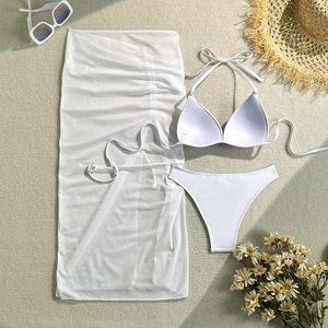 Flat lay of white 3-piece bikini set with sheer mesh sarong and beach accessories