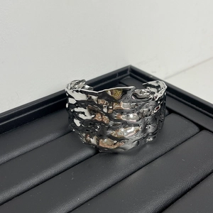 Close-up of a wide silver C-shaped cuff bracelet with a hammered texture on a black display
