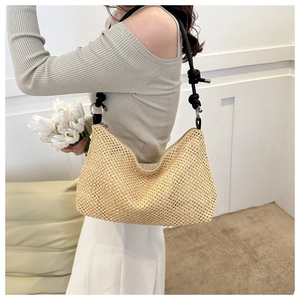 Detail of woven straw tote bag with black shoulder strap and silver metal rings