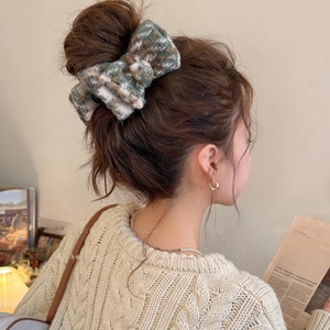 Detail of a plush camouflage bow hair claw clip worn with an autumn knit sweater