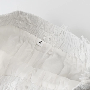 Detailed close-up of white shorts waist with elastic band and floral 3D embroidery detail