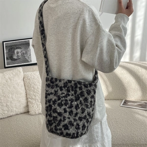 Detail view of a soft leopard print plush bucket bag worn on the shoulder in a cozy room