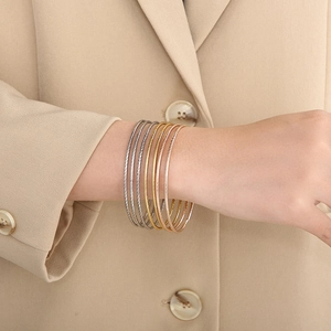 Dettaglio di sei bracciali rigidi sovrapposti in oro, argento e oro rosa con trama a spirale