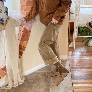 Close-up of beige suede clogs with adjustable buckle worn with brown socks and corduroy pants