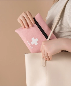 Close-up of pink first aid pouch being pulled from a beige tote bag for travel use