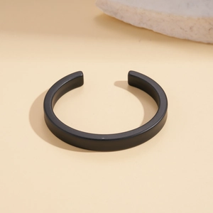 Detail view of a black matte acrylic geometric cuff bracelet on a beige stone surface