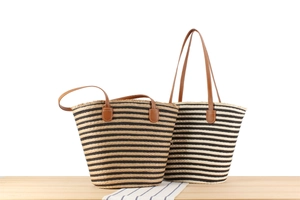 Detail of woven straw tote bags with striped patterns and brown leather handles on wood