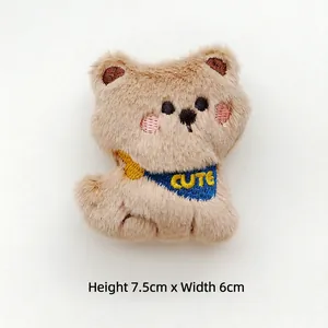 Close-up of cute brown plush bear brooch with blue scarf and embroidered CUTE lettering