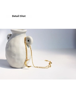 Detail shot of a gold crescent moon pendant necklace with textured surface on a ceramic vase