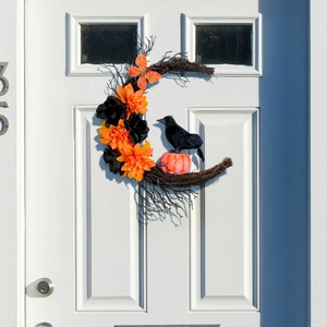 Couronne de lune Halloween avec corbeau noir, fleurs oranges et citrouilles sur porte blanche